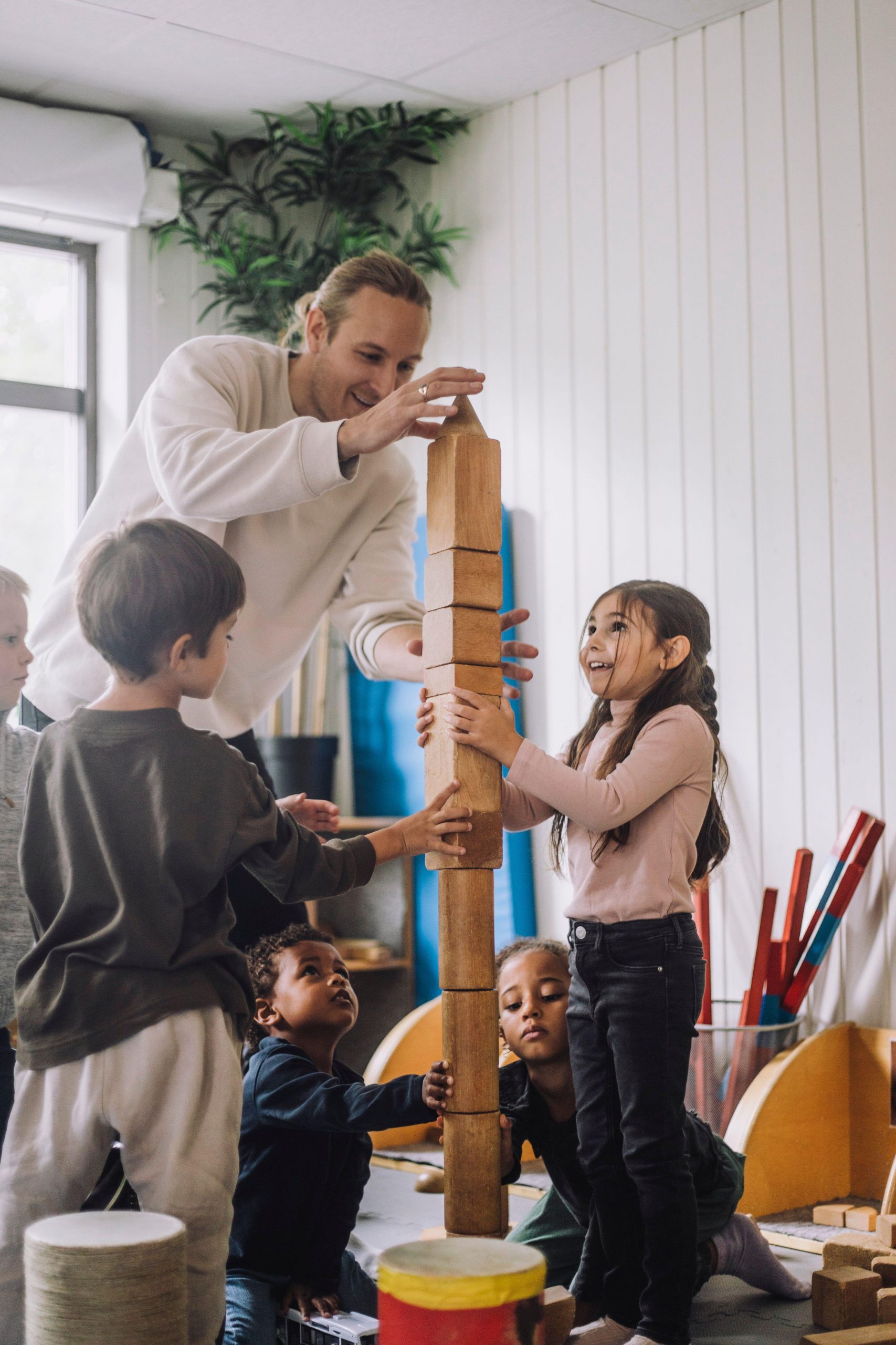 Betreuungsperson baut mit Kindern einen Turm aus Bauklötzen.