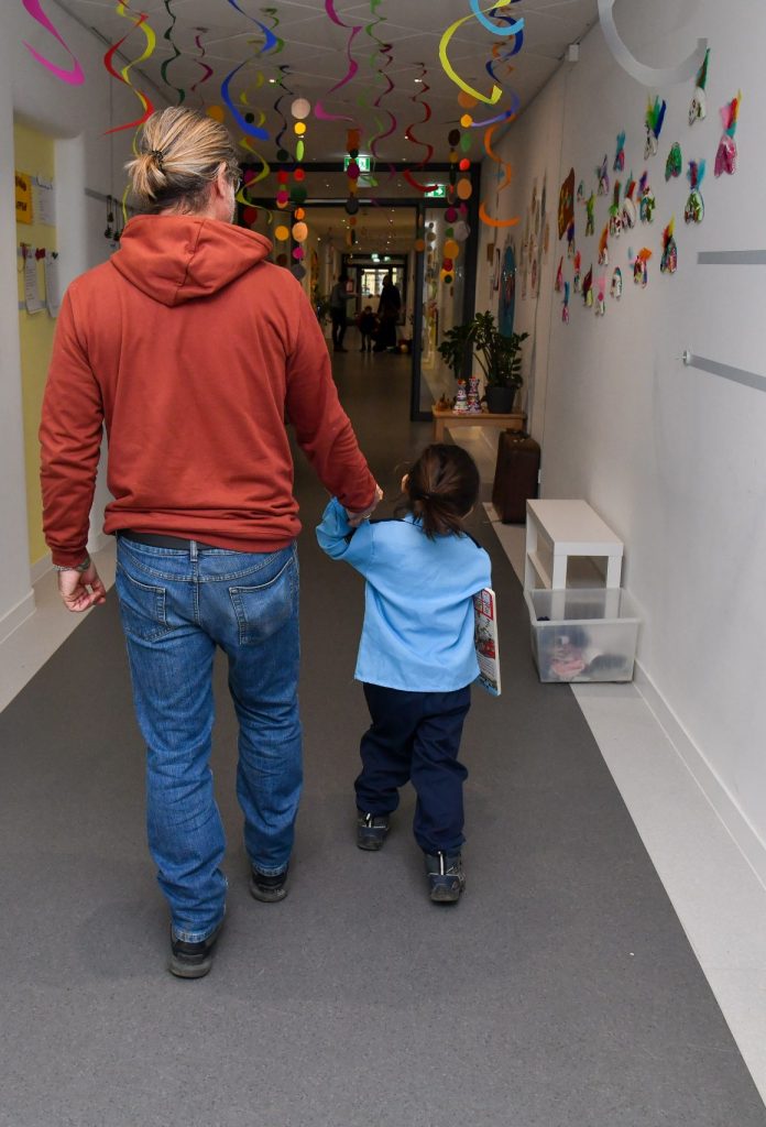 Kind und Betreuungsperson von Hinten auf Kita-Flur