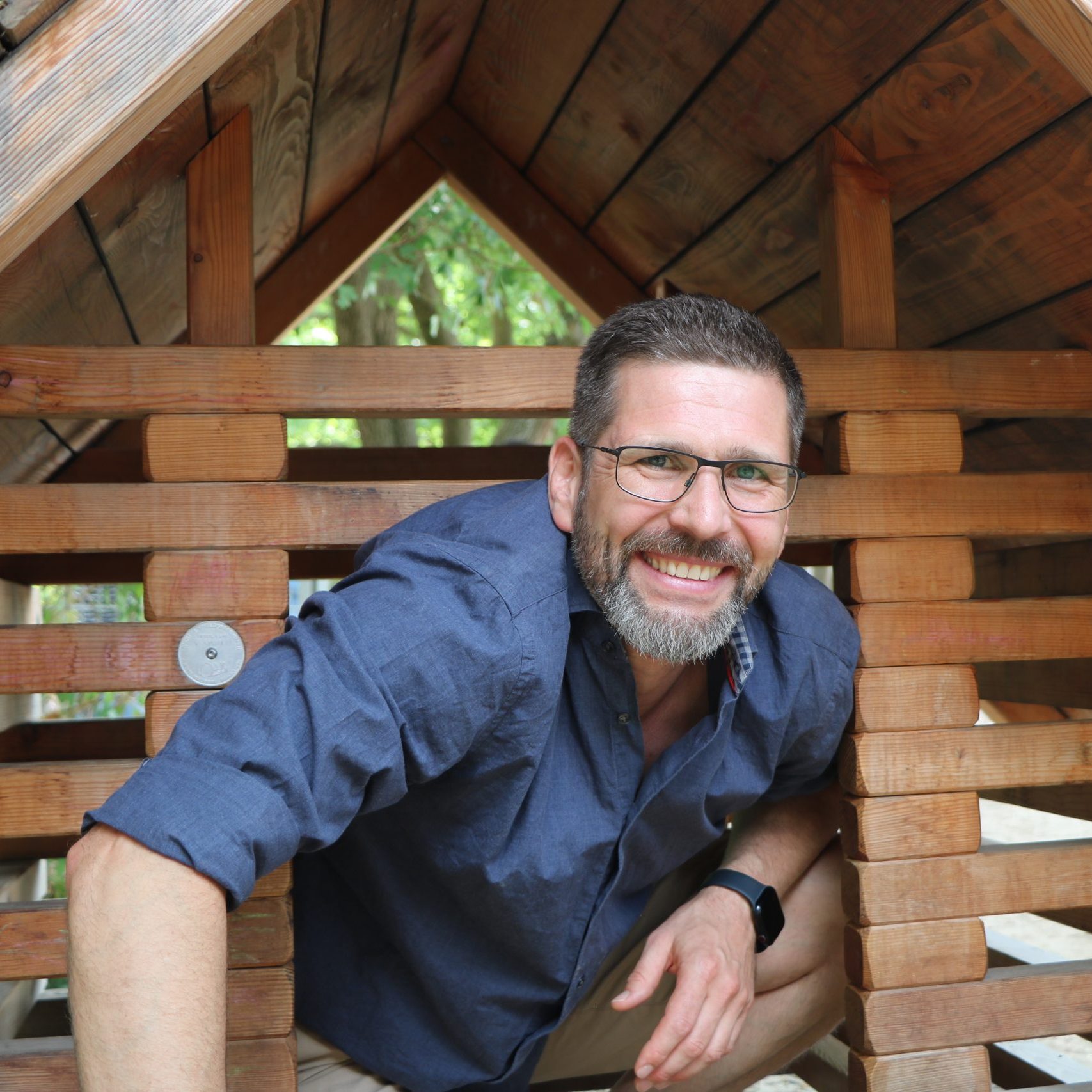 Mann in Kinder-Spielhaus, lächelnd.